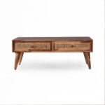 Handcrafted Sheesham wood and cane coffee table with natural finish, two storage drawers, and modern tapered legs in a cozy living room setup.