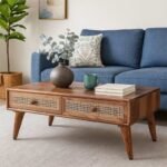 Handcrafted Sheesham wood and cane coffee table with natural finish, two storage drawers, and modern tapered legs in a cozy living room setup.