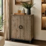 Carved wooden bar cabinet with sunburst-pattern doors, circular centre handle, distressed wood finish, and black metal base.